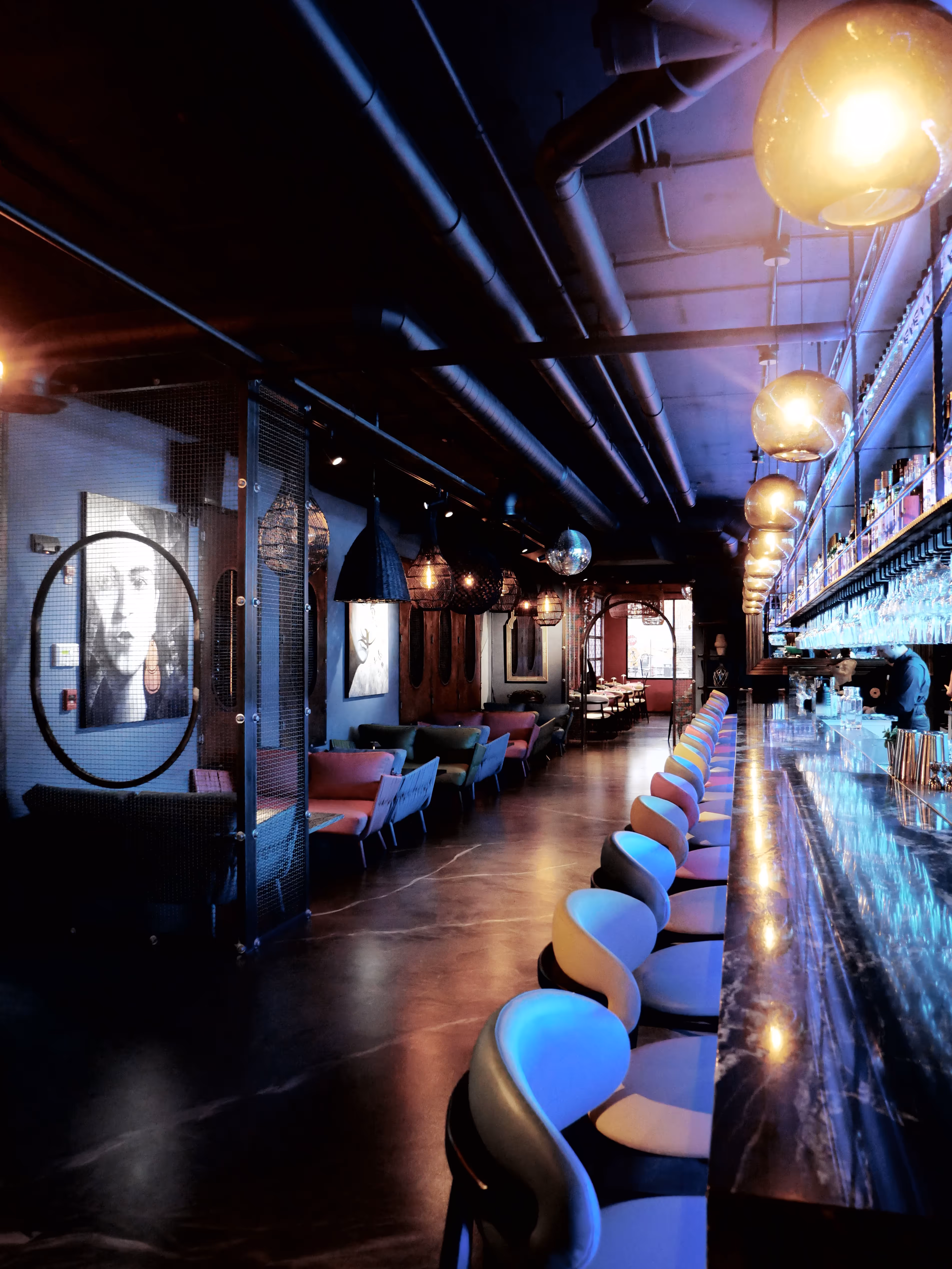 Modern bar interior with a long marble counter and rows of illuminated bar stools under hanging globe lights.
